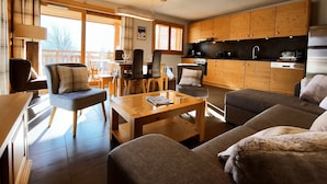 A modern living room with a sofa, armchairs, and a dining table. There is a kitchen area with wooden cabinets and a built-in oven. - Bright T3 apartment for 4-6 people with WIFI and parking in Samoëns (Samoëns)