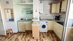 Une cuisine compacte avec un plancher en bois, un lave-linge, un évier et un petit tabouret.