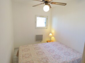 A bedroom with a bed, a ceiling fan, a window, and a nightstand with a lamp.