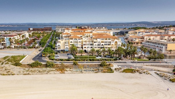 Um hotel à beira-mar com vários edifícios, uma praia de areia e vista clara do oceano.