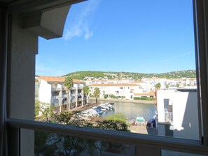 A view of a marina with boats docked, a body of water, and buildings in the background.