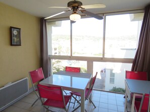 A dining area with a table and chairs, a ceiling fan, and large windows with a view of the outside.