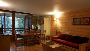 A cozy living room with a wooden floor, a red sofa, a wooden coffee table, and a dining area with wooden chairs and a table. - Brides-les-Bains: 3-Room Apartment, Parking, Pets Allowed, Wifi (Brides-les-Bains)
