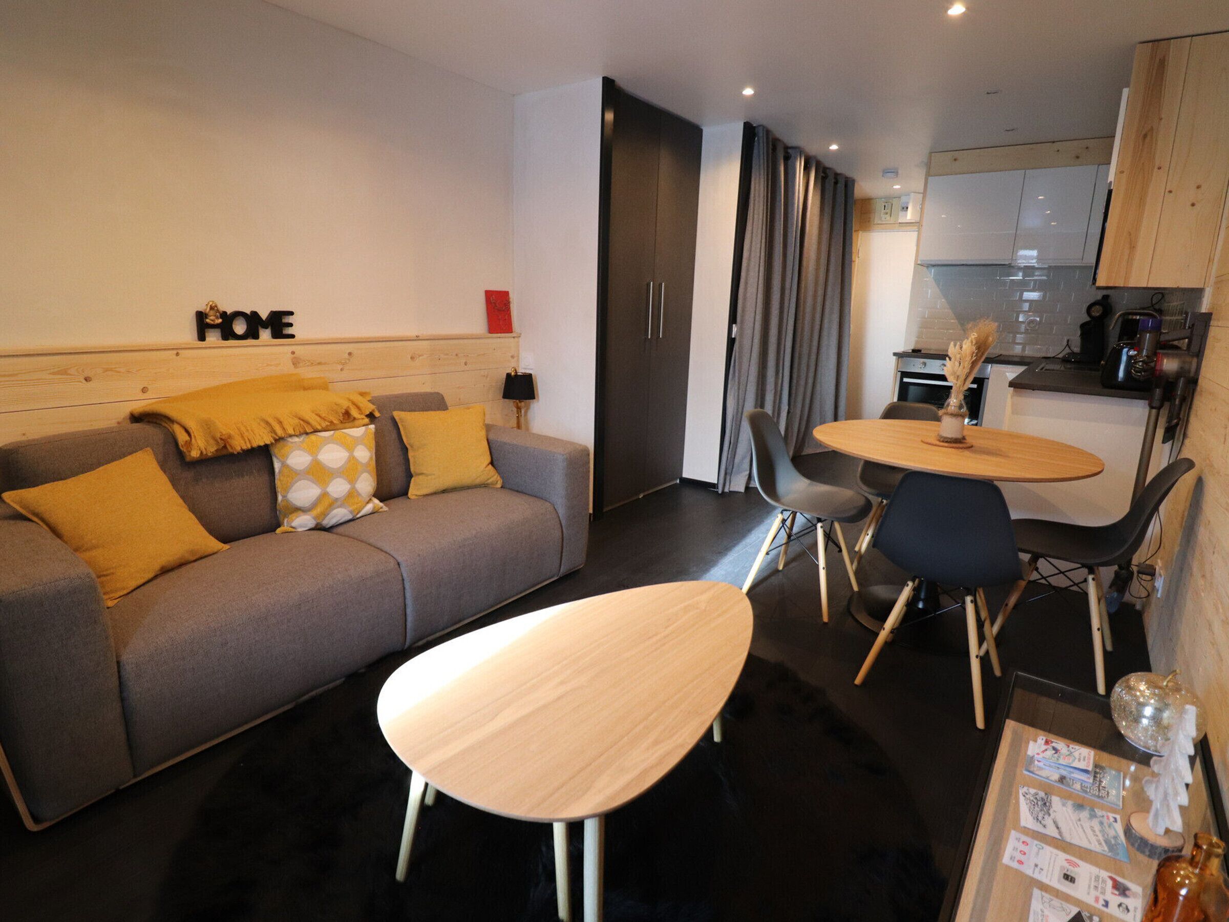 A modern living room with a grey sofa, a wooden coffee table, and a small dining area with a round table and chairs.