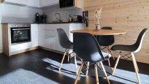 A modern kitchen with white cabinets, a built-in oven, and a wooden dining table with black chairs.