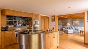 A modern kitchen with wooden cabinets, stainless steel appliances, and a central island. - Luxury Beachfront cottage only 20 steps from the sand with private parking/patio (Portreath)