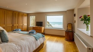 A bedroom with a bed, wooden wardrobe, dresser, and a view of the ocean. - Luxury Beachfront cottage only 20 steps from the sand with private parking/patio (Portreath)