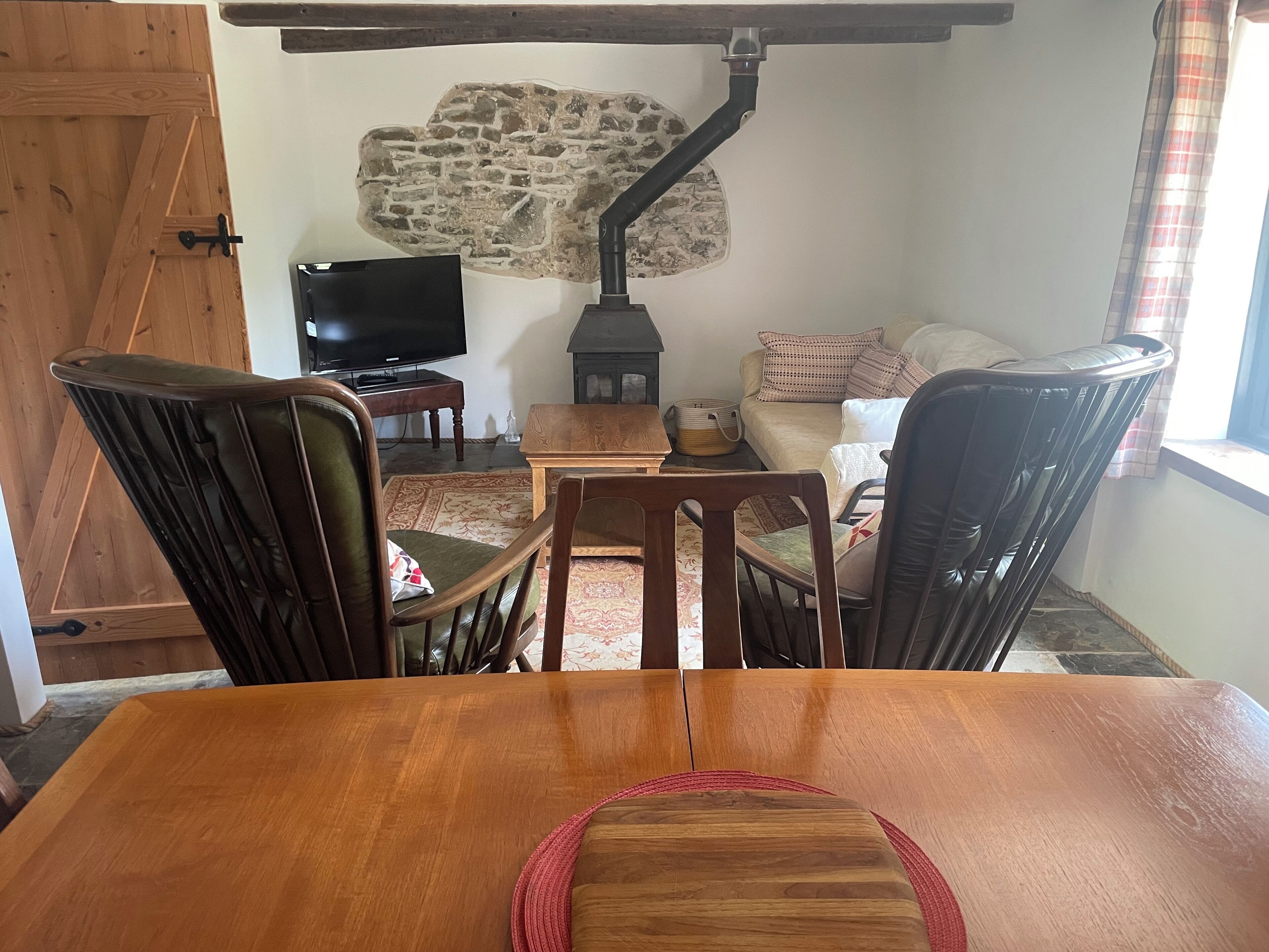 Een eetgedeelte met een houten tafel en stoelen, een televisie, een stenen muur en een bank met kussens.