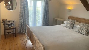 A bedroom with a bed, a chair, a small table, and a window with curtains.