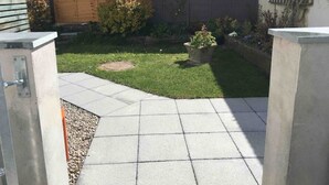 A small, well-maintained garden with a paved patio area, a wooden fence, and a concrete wall.