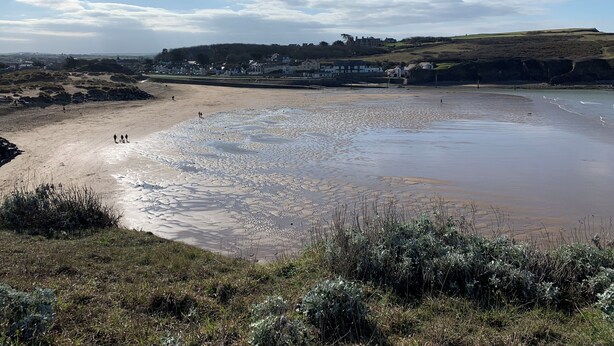 A coastal beach with a sandy shore and a few people walking.