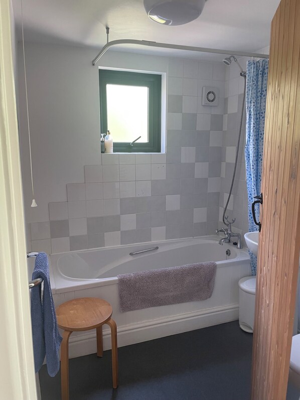 Een badkamer met een bad, een raam, een douche, een wastafel en een houten kruk.