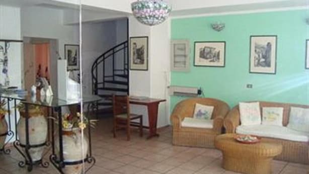 Un salon avec un escalier, des meubles en osier et des tableaux encadrés accrochés aux murs.