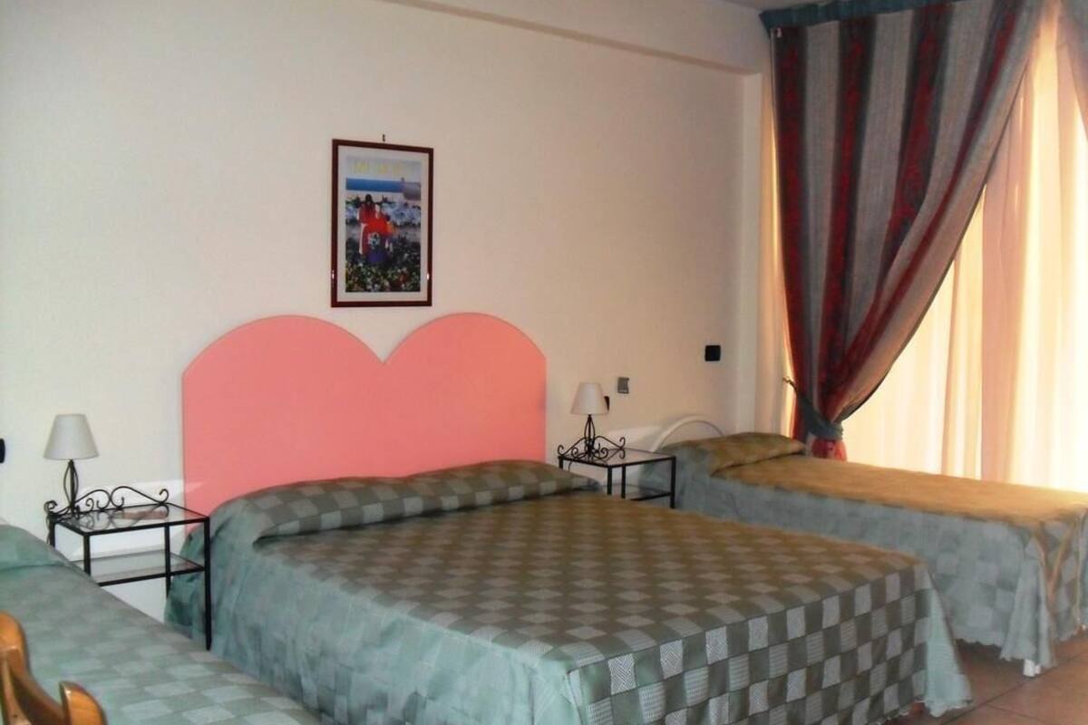 A room with two beds, a large heart-shaped headboard, a framed picture on the wall, and a window with curtains.