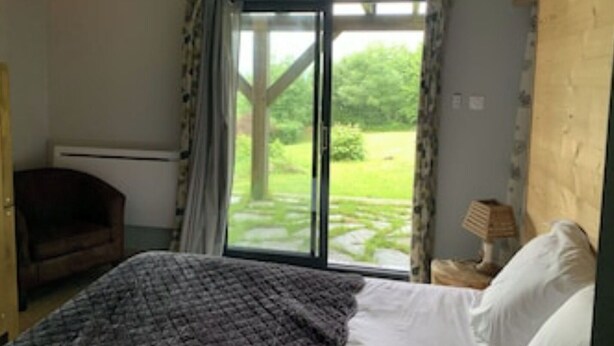 Un dormitorio con cama, una silla, una lámpara y vistas a un jardín por un ventanal corredero.