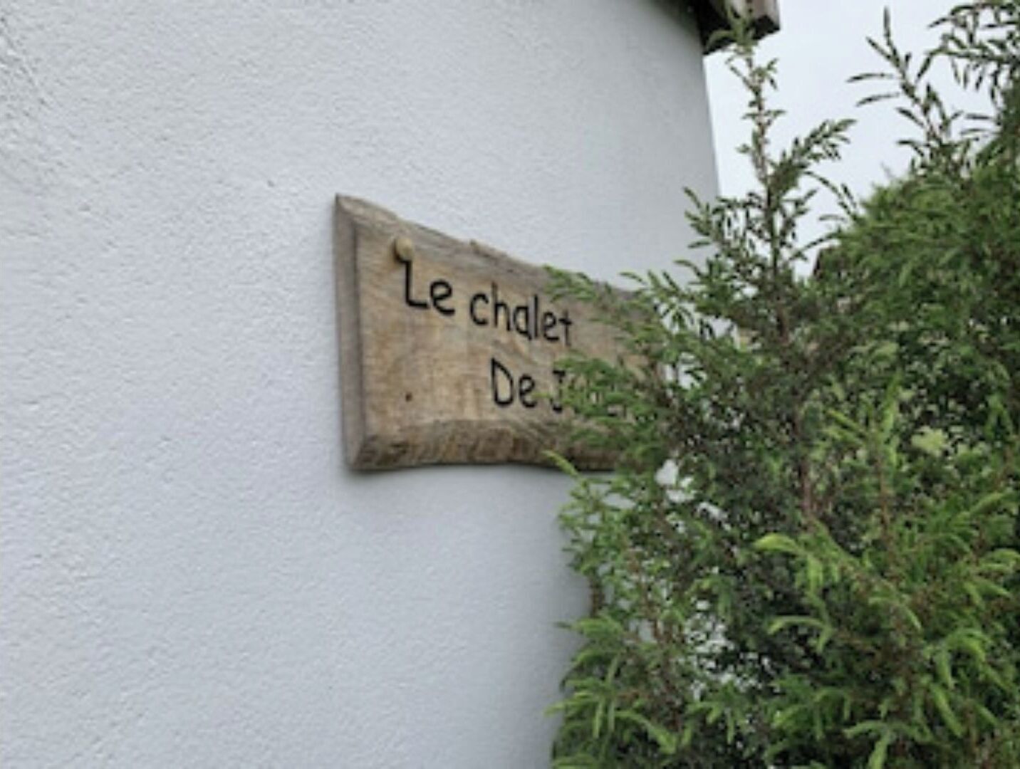 A wooden sign with the text "Le chalet De J." mounted on a white wall.