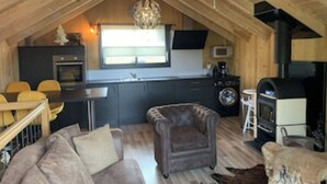 Una habitación estilo loft acogedora, con techo de madera, un sofá, una silla, una mesa de comedor y una kitchenette.