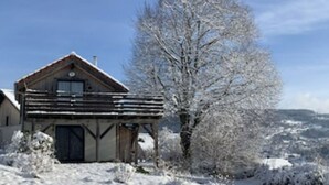Una cabaña de madera con balcón, rodeada de árboles cubiertos de nieve y un cielo despejado.