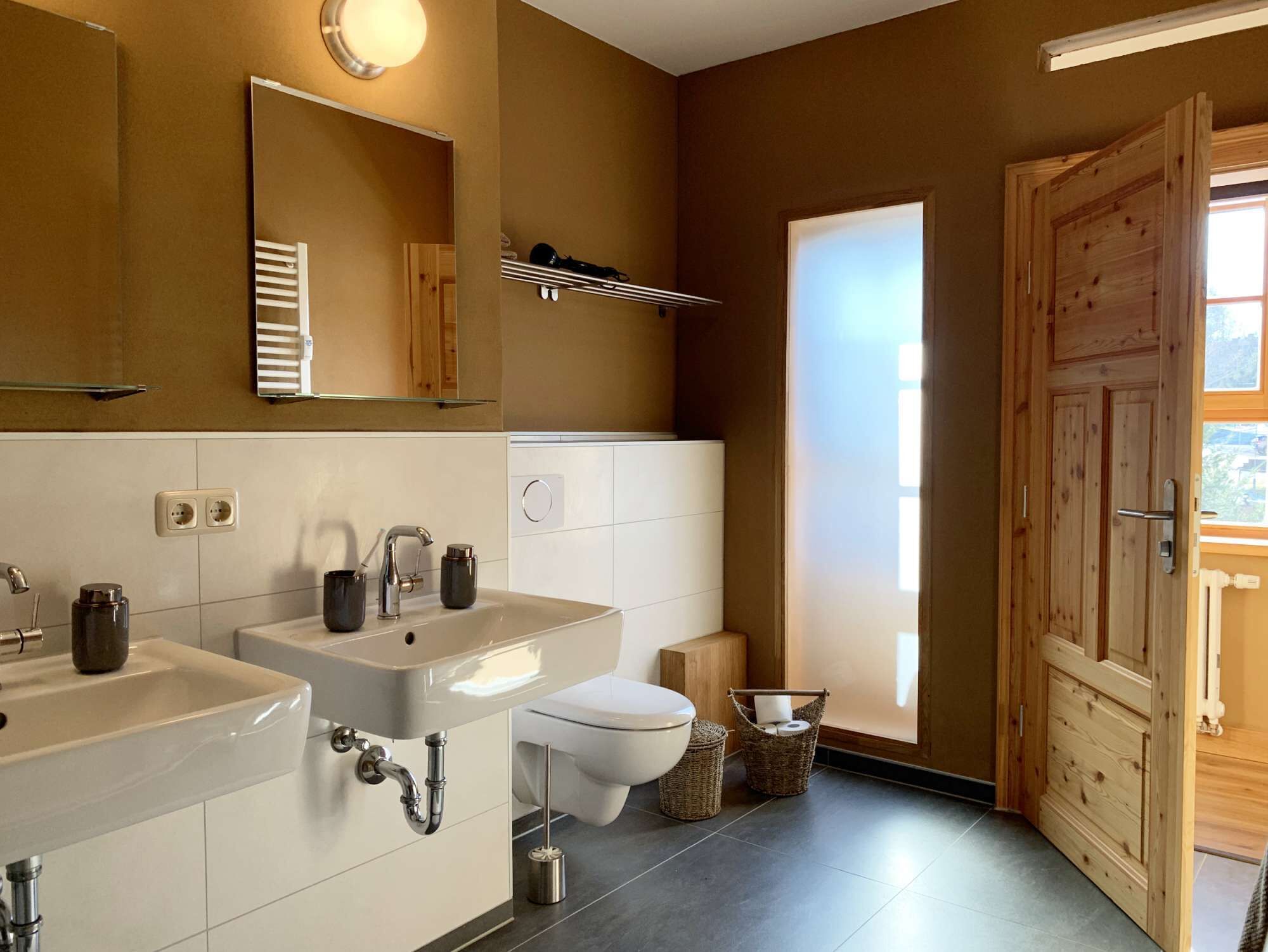 A modern bathroom with two sinks, a toilet, and a large mirror.