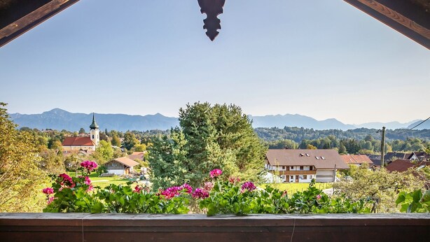 A wooden balcony with a view of a village, a church, and mountains. - Spacious, renovated farmhouse in its own garden (Seehausen am Staffelsee)
