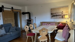 A cozy living room with a sofa, wooden chairs, a dining table, and a fireplace. - Spacious, renovated farmhouse in its own garden (Seehausen am Staffelsee)