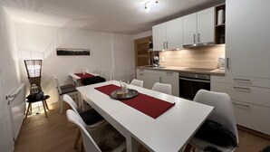 A modern kitchen with white cabinets, a dining table with chairs, and a red placemat. - Spacious, renovated farmhouse in its own garden (Seehausen am Staffelsee)