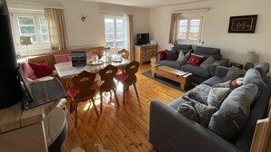 A cozy living room with a grey sofa, wooden coffee table, and a dining area with a table and chairs. - Spacious, renovated farmhouse in its own garden (Seehausen am Staffelsee)