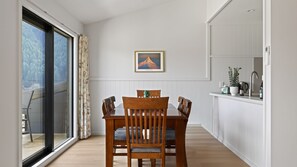 A dining area with a wooden table and chairs, a view through a glass door, a framed picture on the wall, and a kitchen area with a sink and cabinets. - Magic on Malaghan with Lake Views (Queenstown)