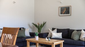 A living room with a dark blue sofa, a wooden coffee table, and a potted plant. - Magic on Malaghan with Lake Views (Queenstown)