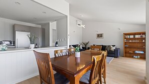 A modern kitchen with a dining area, a living room with a sofa and a bookshelf, and a ceiling with recessed lighting.