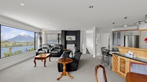 A modern living room with leather sofas, a wooden coffee table, and a view of a lake and mountains. - Wonderful On Woodlands - Family friendly home (Queenstown)