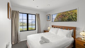 A hotel room with a large bed, a window with curtains, a bedside table with a lamp, and a framed picture on the wall. - Wonderful On Woodlands - Family friendly home (Queenstown)