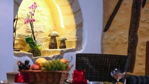 A dining area with a stone wall, a wicker chair, a table with a basket of fruit, a red candle, and a glass of wine. - Awesome home in Sarlat-la-Canéda with WiFi (Sarlat-la-Canéda)