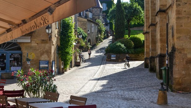 A cobblestone street with outdoor seating, historic buildings, and a cyclist in the distance. - Awesome home in Sarlat-la-Canéda with WiFi (Sarlat-la-Canéda)