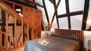 A bedroom with a sloped ceiling, wooden beams, a bed with a grey bedspread, a small bedside table with a lamp, and a chair. - Awesome home in Sarlat-la-Canéda with WiFi (Sarlat-la-Canéda)