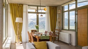 Un comedor con una mesa preparada para dos personas, un sofá y vistas a la montaña a través de amplios ventanales.