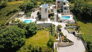 Una villa moderna con piscina, rodeada de exuberante vegetación y terreno montañoso.
