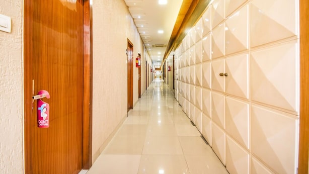 Un couloir d’hôtel avec des portes en bois sur le côté gauche et des murs recouverts de carreaux sur le côté droit.
