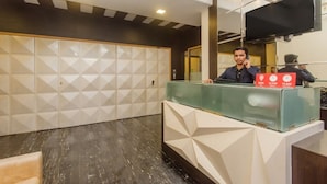 Un comptoir d’accueil avec une cloison en verre, une horloge numérique indiquant 12 h 00, et un téléviseur à écran plat fixé au mur.