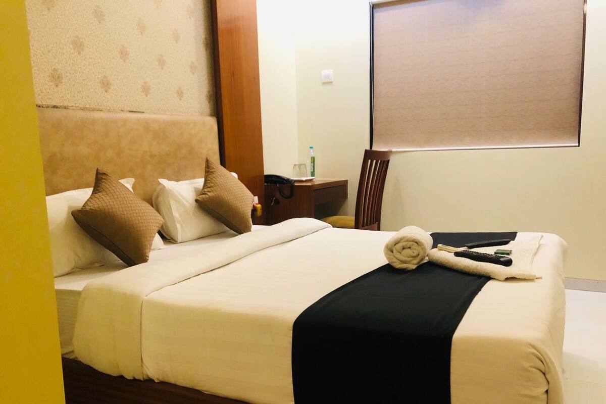 A hotel room with a bed, pillows, a blanket, a rolled towel, a nightstand with a phone, a bottle, and a chair.