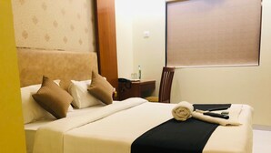 Une chambre d’hôtel avec un lit, des oreillers, une couverture, une serviette enroulée, une table de chevet avec un téléphone, une bouteille et une chaise.