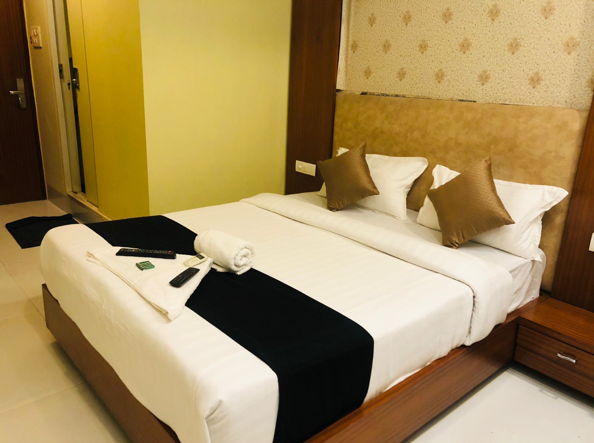 Een hotelkamer met een groot bed, een houten hoofdbord, een nachtkastje en een badkamer met spiegel en toilet.