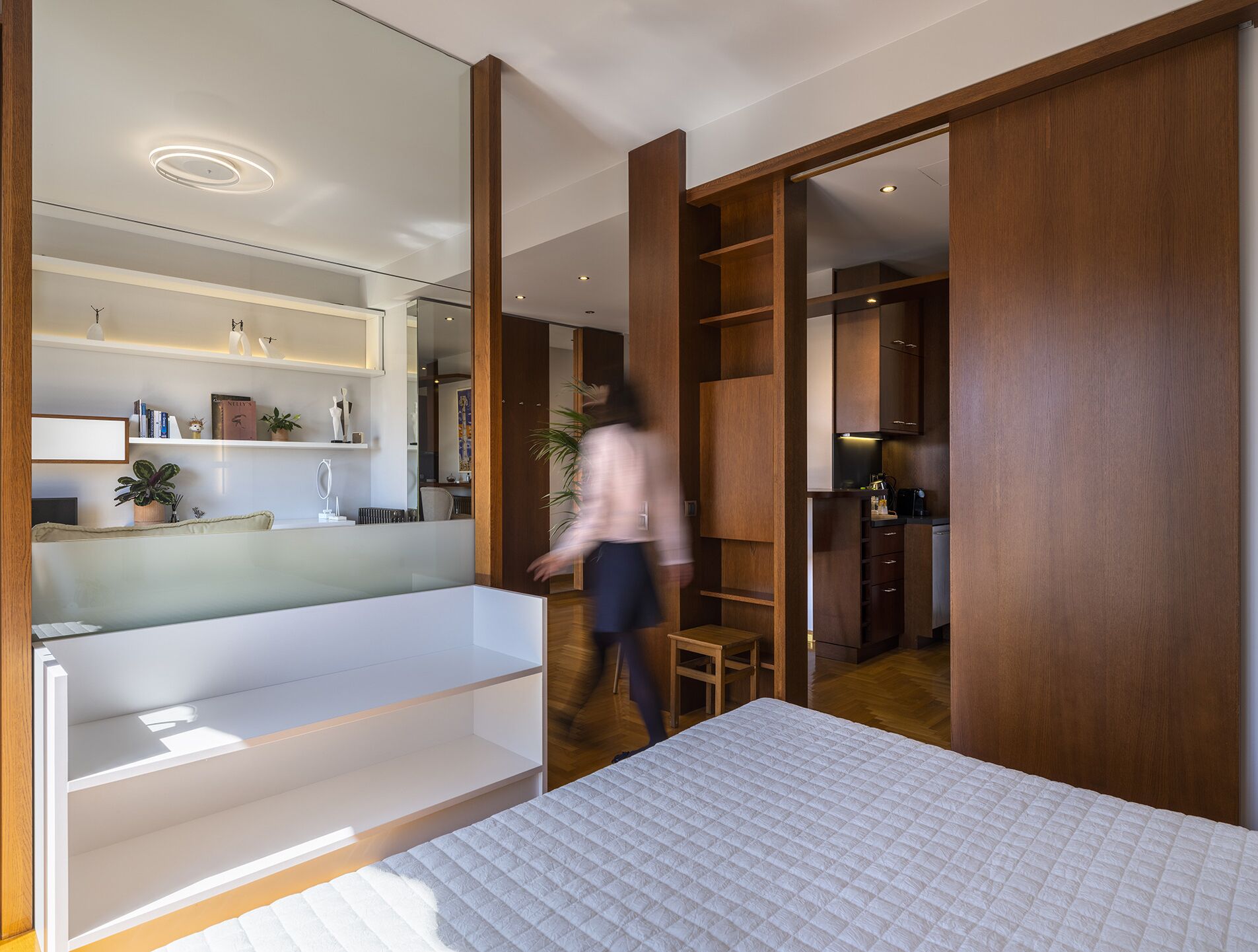 Un dormitorio moderno con una cama grande, un vestidor y una cocina visible a través de una puerta abierta.