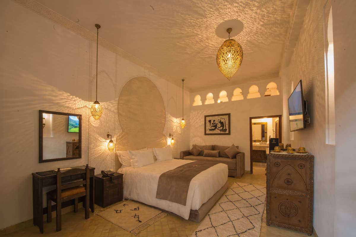 A spacious bedroom with a large bed, a desk, a television, and decorative wall sconces.