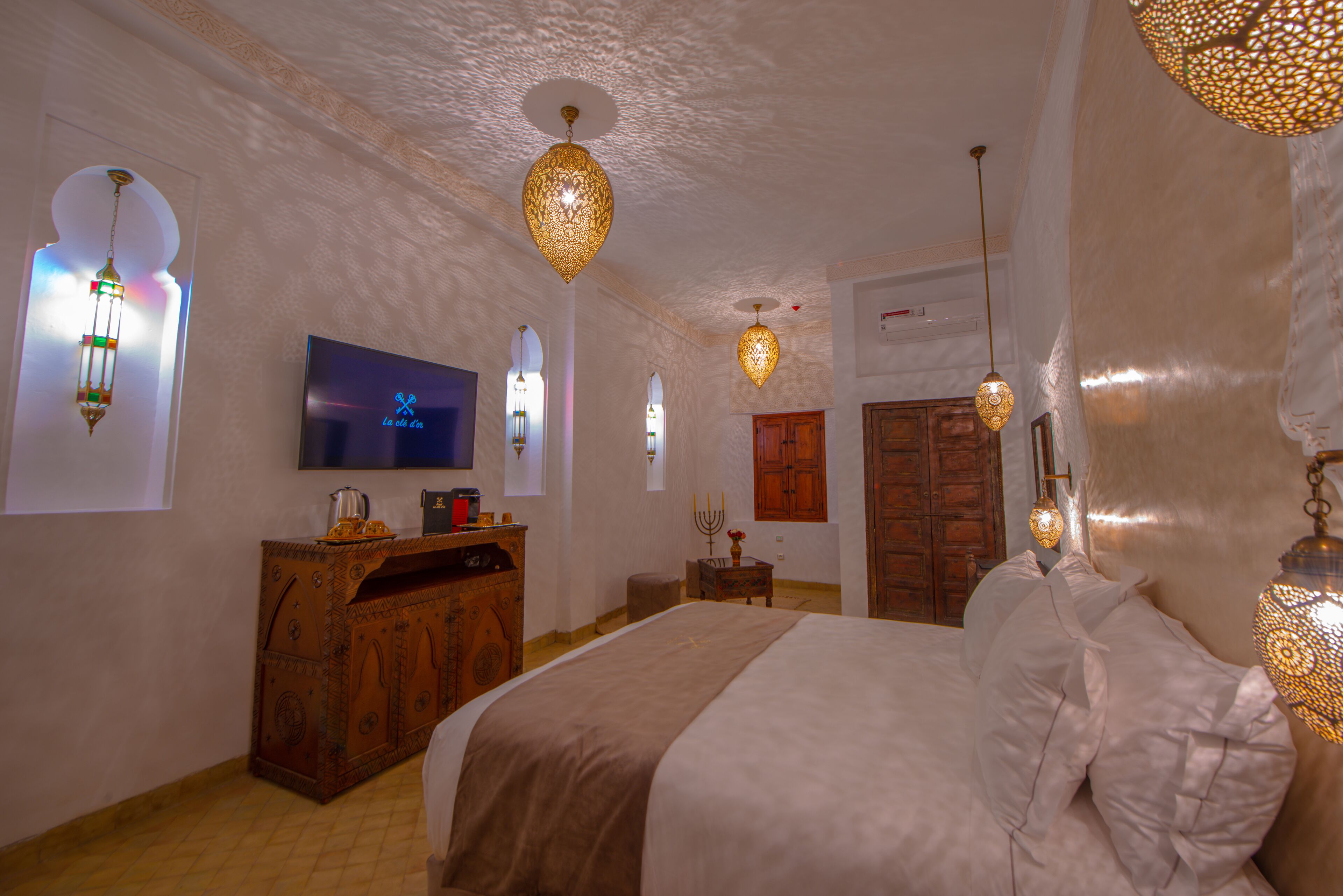 A bedroom with a large bed, a television, a wooden dresser, and decorative wall sconces.