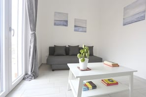 A modern living room with a grey sofa, a white coffee table with books, and a potted plant.