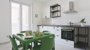 A modern kitchen with white cabinets, a black countertop, and a dining table with green chairs. - GuestHost - Bright & Central Apartment 5 min from the station (Salerno)