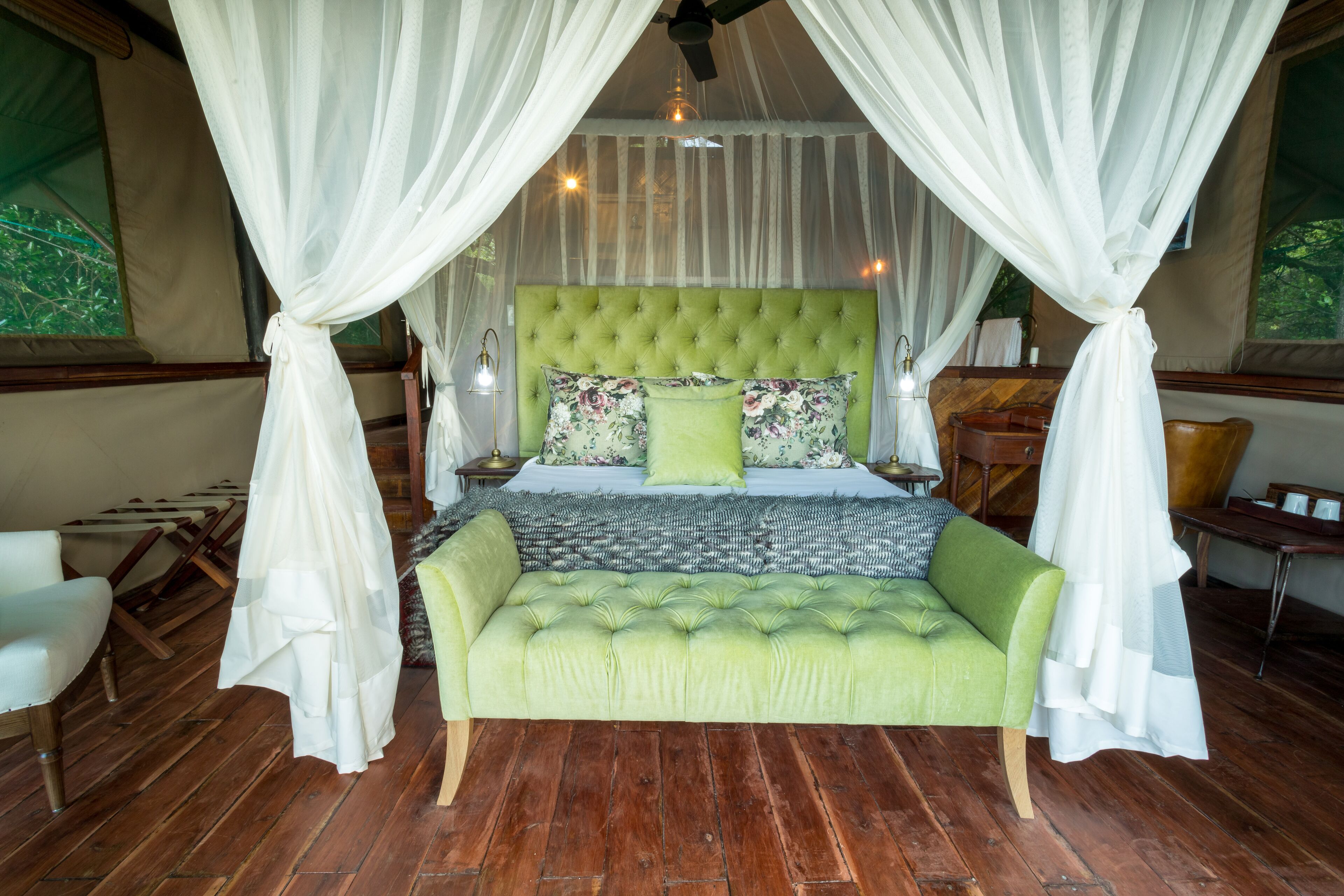 Un dormitorio con un cabecero verde capitonado, almohadas estampadas y un sofá verde.