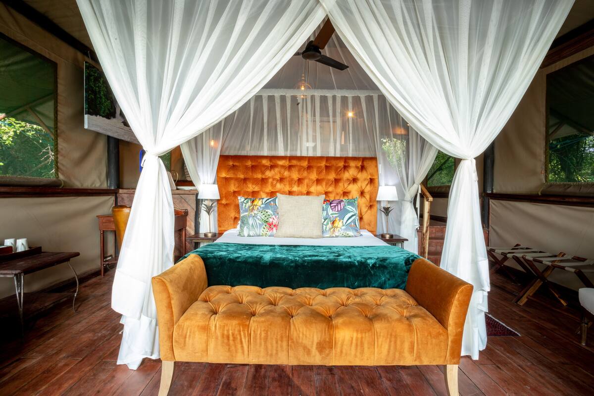 A bedroom with a large bed, a canopy, a sofa, and a wooden floor.