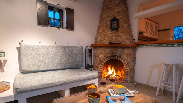 Ein gemütliches Wohnzimmer mit Kamin aus Stein, einer Couch und einem Tisch mit Snacks und einem Buch.